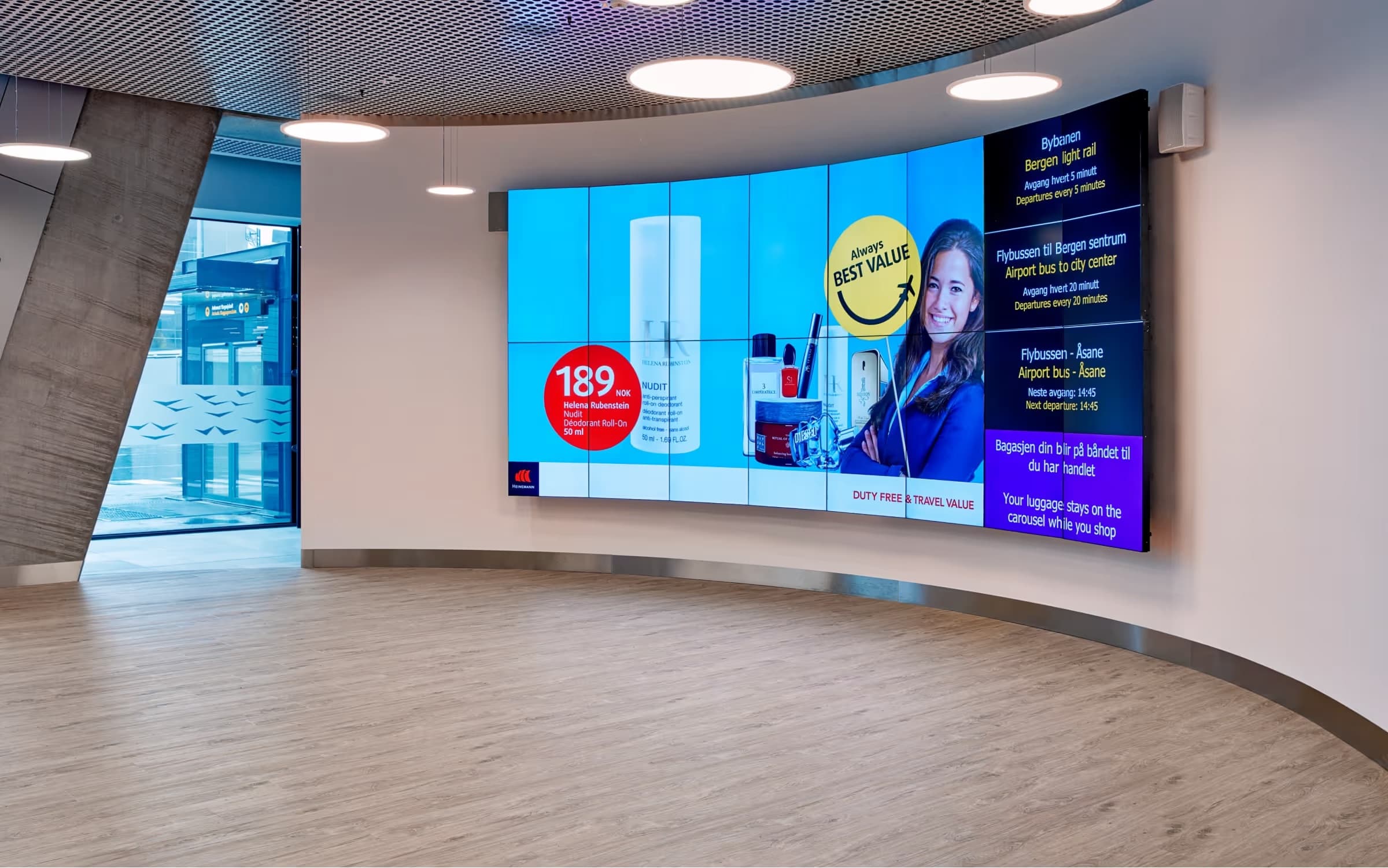 A curved video wall in an airport showing duty free offers beside bus departures