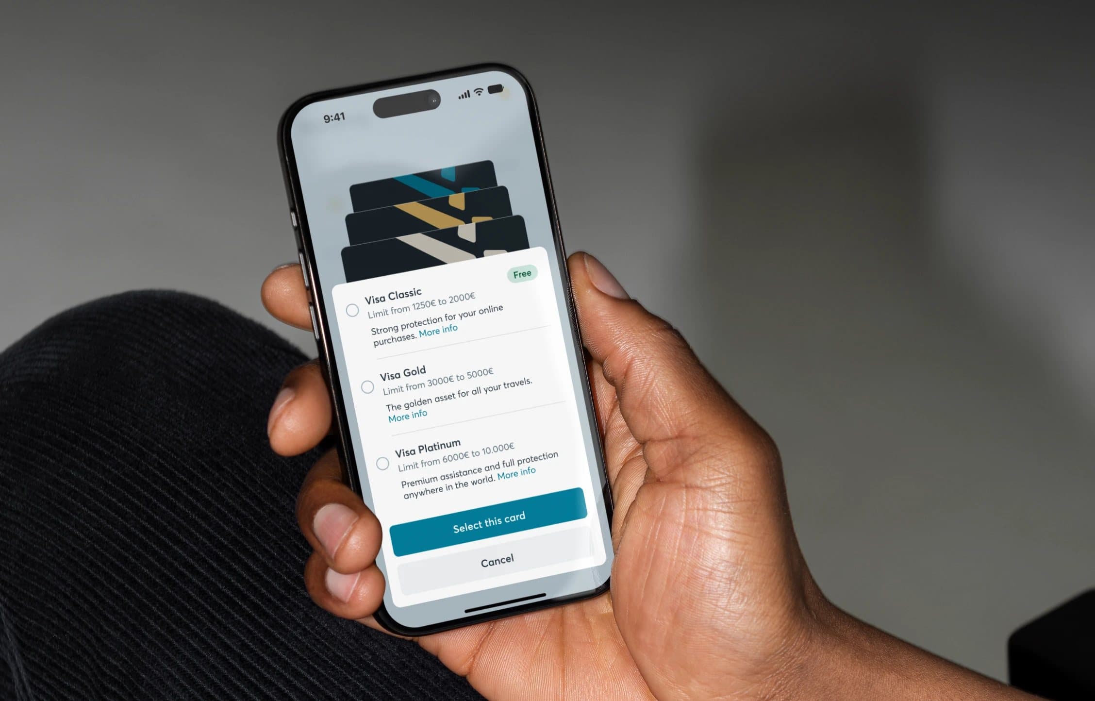 A hand holding a phone with the Keytrade Bank app, choosing between the Visa Classic, Gold and Platinum cards